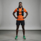 Man wearing an orange shirt, black shorts, and green shoes with a gray background Run With Freedom Challenger Hydration Running Vest Gym Lifestyle Photoshoot