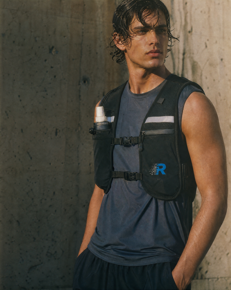 Man wearing a black wearing a Run With Freedom Challenger Vest  with a logo against a concrete wall